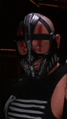 a bald man wearing a mask with the letter t on his chest
