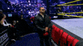 a man in a leather jacket stands in a wrestling ring with a sign behind him that says exit