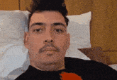 a man with a mustache is laying on a bed and looking at the camera .