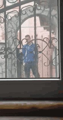 a man in a blue jacket is standing behind a wrought iron fence