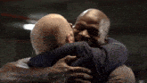 two men hugging each other in a dark room with a light behind them