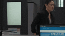 a woman is standing in front of a computer with a gifrun.com watermark on the bottom