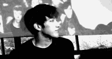a black and white photo of a young man standing in front of a wall with a picture of a group of people on it .