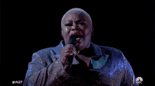 a woman singing into a microphone with #agt on the bottom right