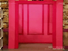 a woman standing in front of a pink door that says rupaul 's drag race on it