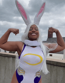 a woman in a bunny costume flexes her muscles in front of a cloudy sky