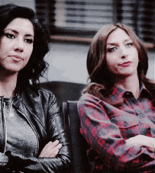 two women are sitting next to each other with their arms crossed and one is wearing a plaid shirt