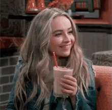a woman is sitting on a couch holding a milkshake with a straw and smiling .