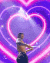 a shirtless man is standing in front of a heart shaped neon sign .