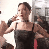 a woman wearing a choker and a black tank top is standing in a room with her arms outstretched .