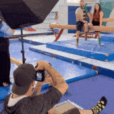 a man is taking a picture of a woman on a balance beam in a gym