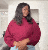 a woman in a red sweater is standing in a living room with her hands folded .