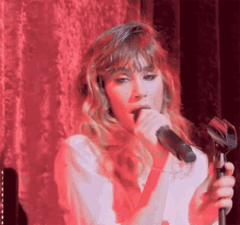 a woman singing into a microphone with a red curtain behind her