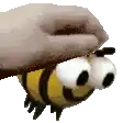 a cartoon bee with big eyes is flying in the air with a person 's hand on its head .