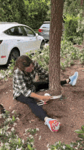 a woman is sitting on the ground stretching her legs next to a tree trunk .