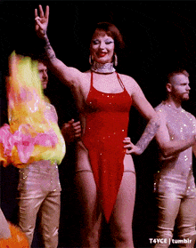 a woman in a red dress is giving a peace sign in front of two men