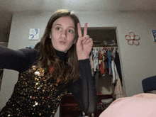 a girl giving a peace sign in front of a closet