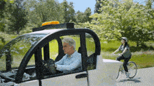 a man is driving a car next to a woman on a bicycle