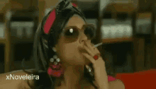 a woman is smoking a cigarette and wearing sunglasses .