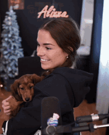 a woman is holding a puppy in front of a sign that says alixa