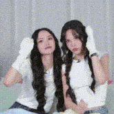 two women with long hair are sitting next to each other on a couch and making funny faces .