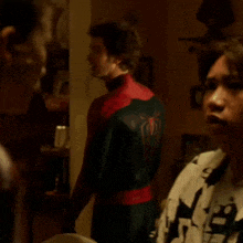 a man in a black and red spiderman suit stands in a dark room