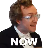 a man wearing glasses and a tuxedo says now