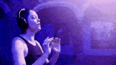 a woman wearing headphones is singing into a microphone in a dark room with purple lights .