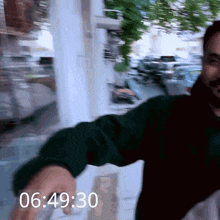 a man in a green jacket is standing in front of a window with the time of 06:49:30