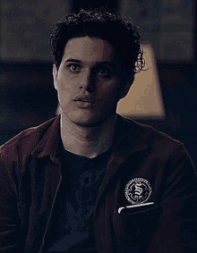 a young man with curly hair is wearing a red jacket and holding a notebook in his pocket .