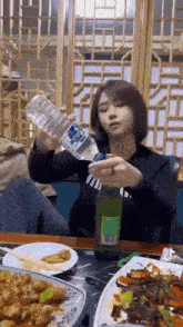 a woman is sitting at a table holding a bottle of water and a bottle of beer .