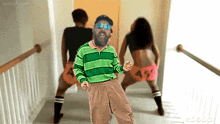 a man in a green striped shirt is dancing with two women in pink shorts