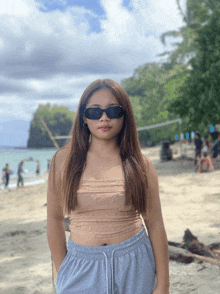 a woman wearing sunglasses and a crop top stands on the beach
