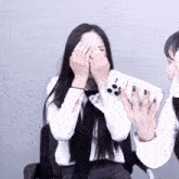 a woman covering her face while another woman holds a phone case