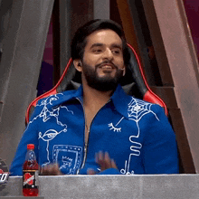 a man in a blue jacket is sitting in a chair next to a bottle of powerade