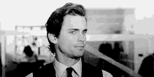 a black and white photo of a man in a suit and tie looking at the camera .