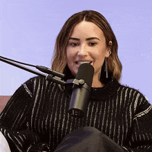 a woman in a black sweater is smiling in front of a black microphone