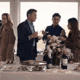 a group of people are gathered around a table with a bottle of wine that says ' a' on it