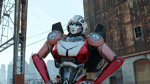a robot with a red and white body is standing in front of a rusty building