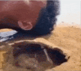 a person is drinking water from a hole in the sand in the desert .