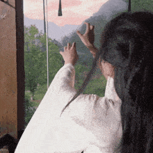 a woman looks out a window with her hands up