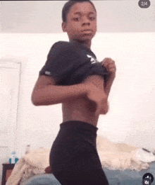 a young boy is standing in a bedroom taking off his shirt and pants .