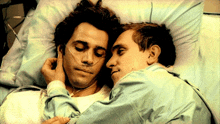 two men laying in a hospital bed with oxygen tubes in their ears