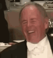 an older man in a tuxedo and bow tie is laughing .