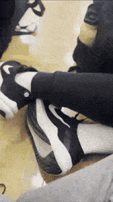 a person wearing black and white nike shoes sits on a wooden floor
