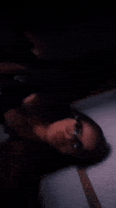 a woman wearing glasses and a black top is laying down in a dark room