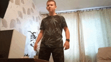 a man in a black shirt with marijuana leaves on it is standing in front of a window