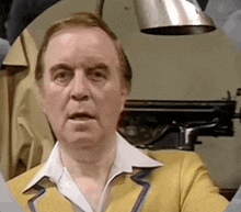 a man wearing a yellow jacket and a white shirt is looking at the camera .