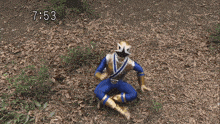 a blue and gold power ranger is sitting on the ground in the leaves .