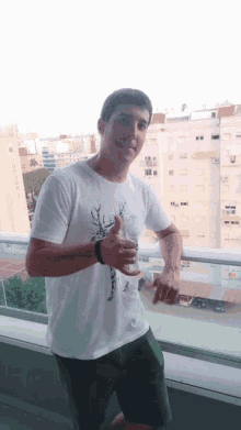 a man wearing a white shirt with a deer on it is standing on a balcony